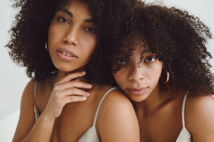 Duas mulheres negras com cabelos cacheados olham para a câmera